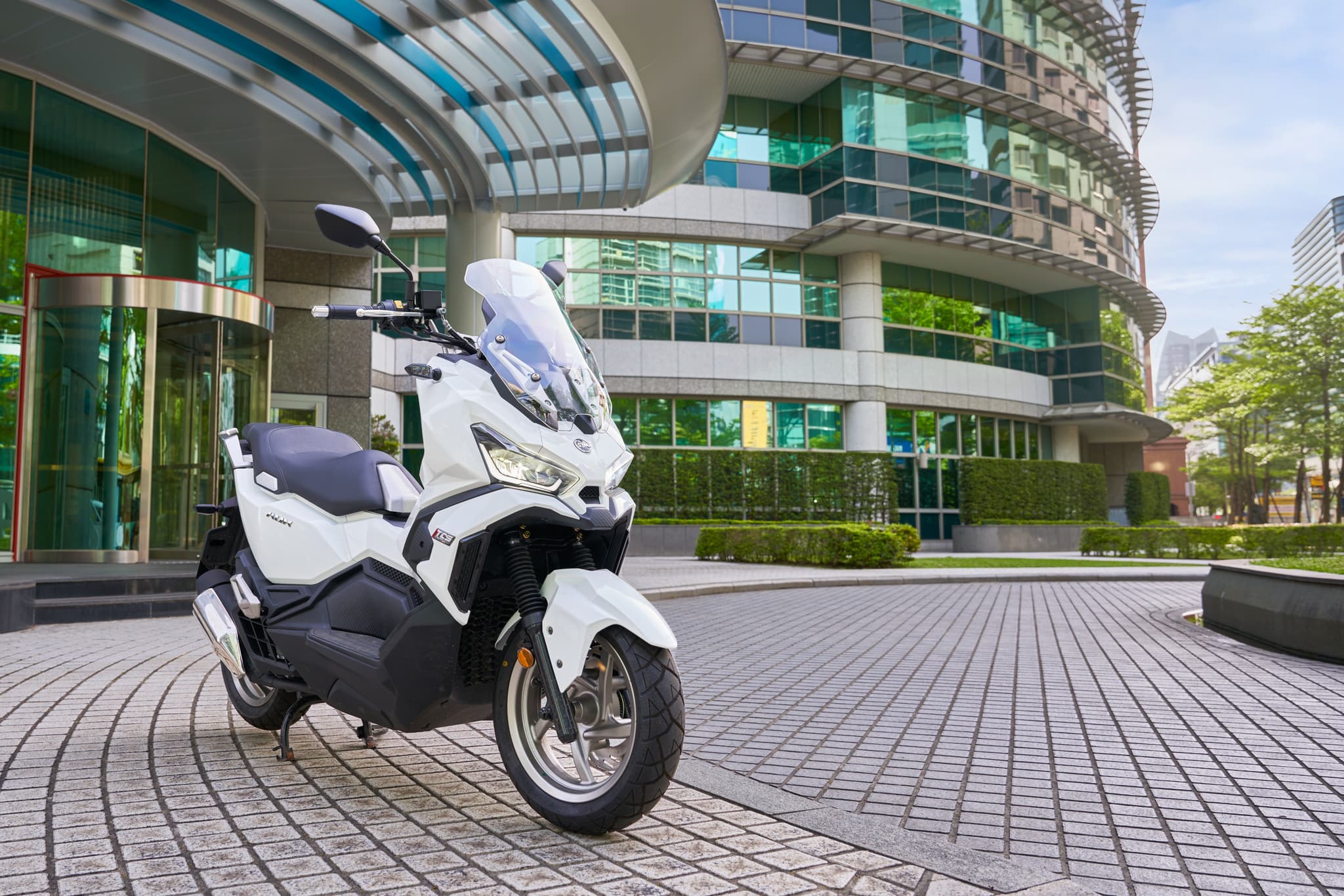 Scooter SYM ADX 125 ABS TCS blanca aparcada frente a un edificio moderno