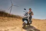 Hombre en scooter SYM ADX 125 ABS TCS blanca en un paisaje desértico con aerogenerador