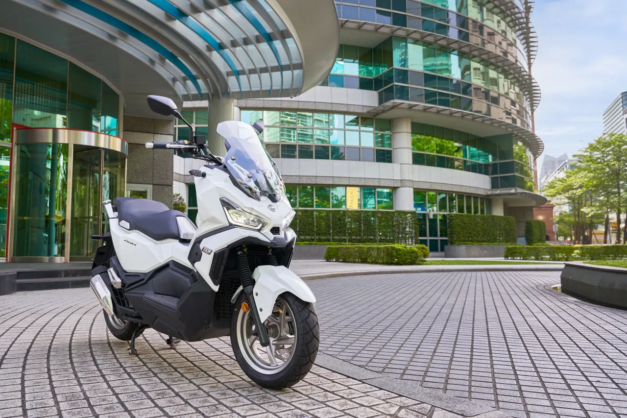 Scooter SYM ADX 125 ABS TCS blanca aparcada frente a un edificio moderno